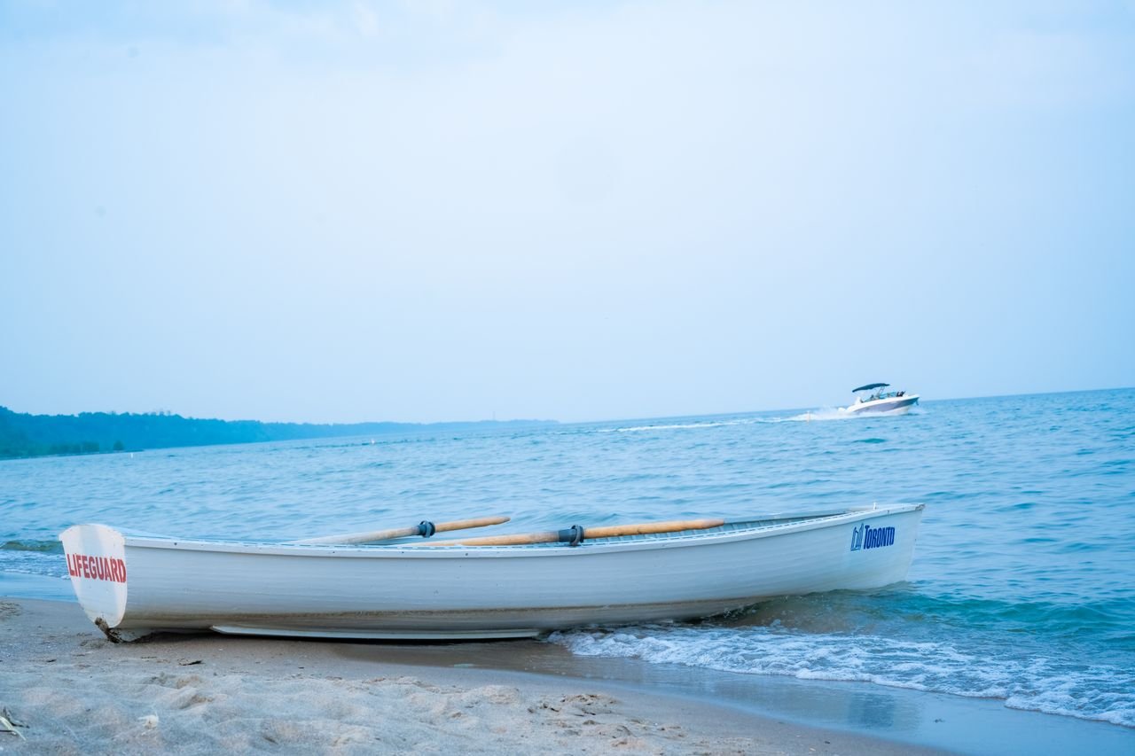 A lifeguard boat rests on a sandy Toronto beach with a distant motorboat on a summer day.