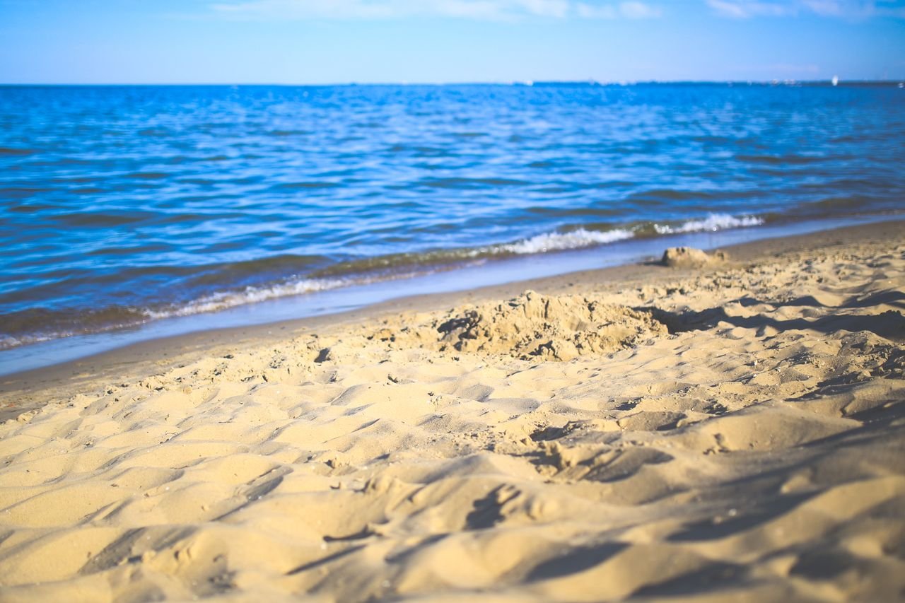 Relaxing sandy beach image with gentle ocean waves under a clear blue sky, perfect for vacation themes.