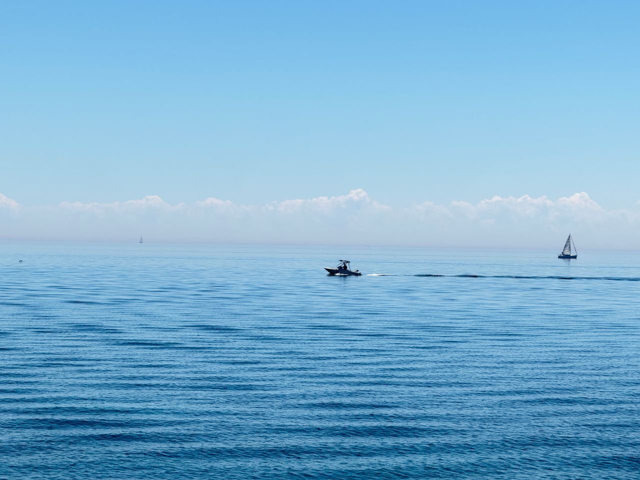 Services A tranquil lake scene featuring a distant speedboat and sailboat under a clear blue sky.